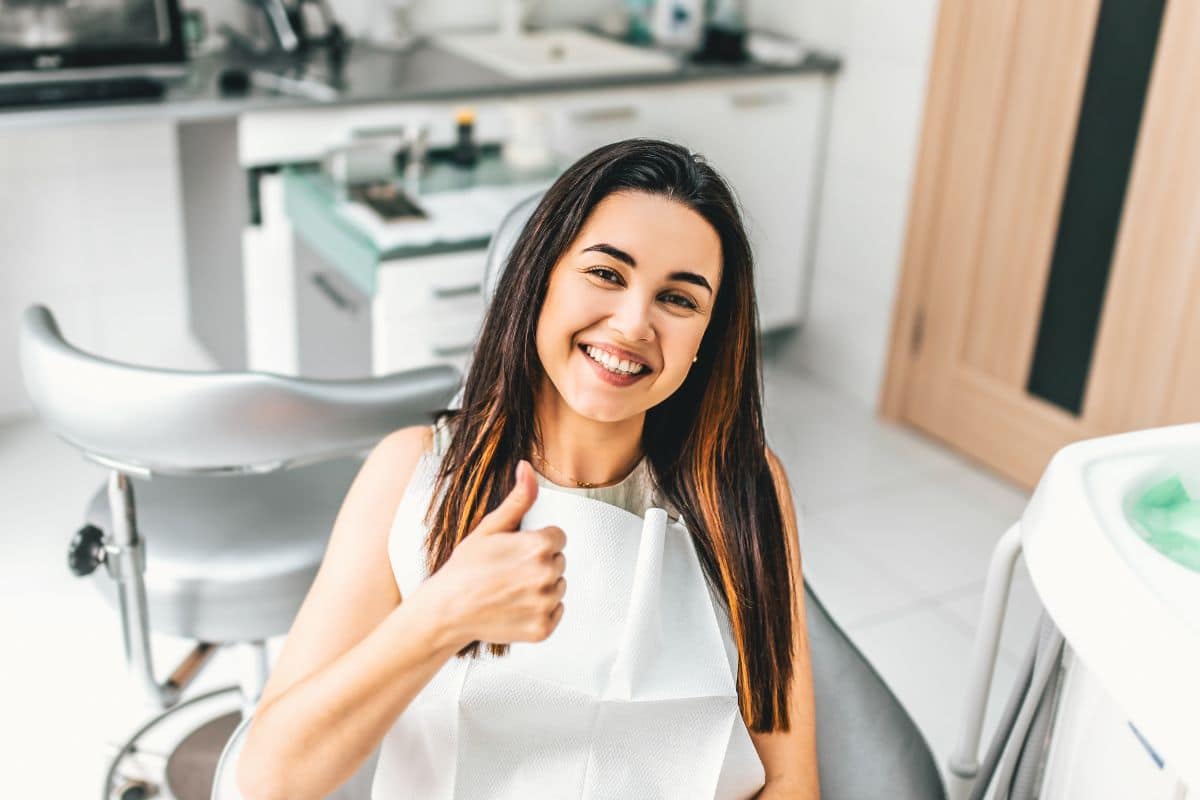 Mujer sonriente en el dentista, mostrando pulgar arriba.